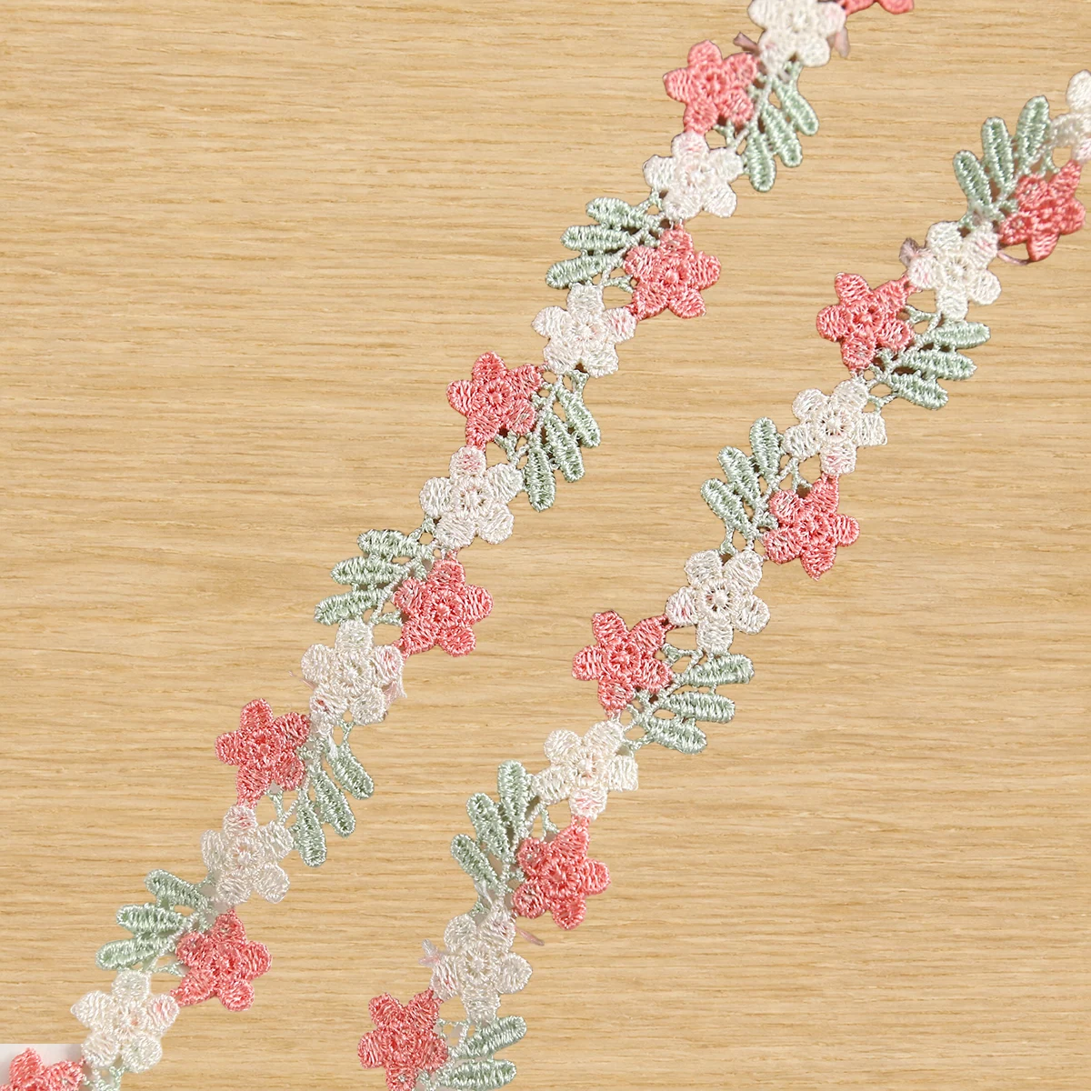 Soft pastel linked blossoms lace trim — Photographed decorative trim sample; verify colour and construction with a physical sample