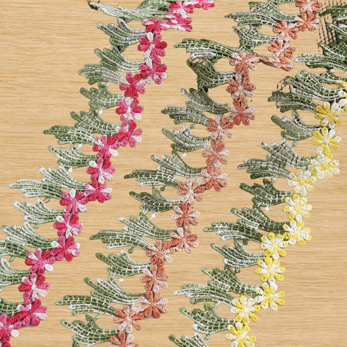 Pink and green leaf vine lace trim — Photographed decorative trim sample; verify colour and construction with a physical sample